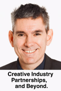 A professional headshot of a smiling middle-aged man in a dark suit and patterned shirt with a tie. Bold text is added below his chin that reads: Creative Industries Partnerships, and Beyond.